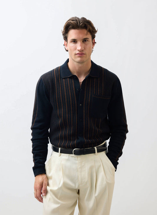 A model wears the Percival Appendix Long Sleeve Knitted Shirt in black with brown stripes, paired with cream trousers.