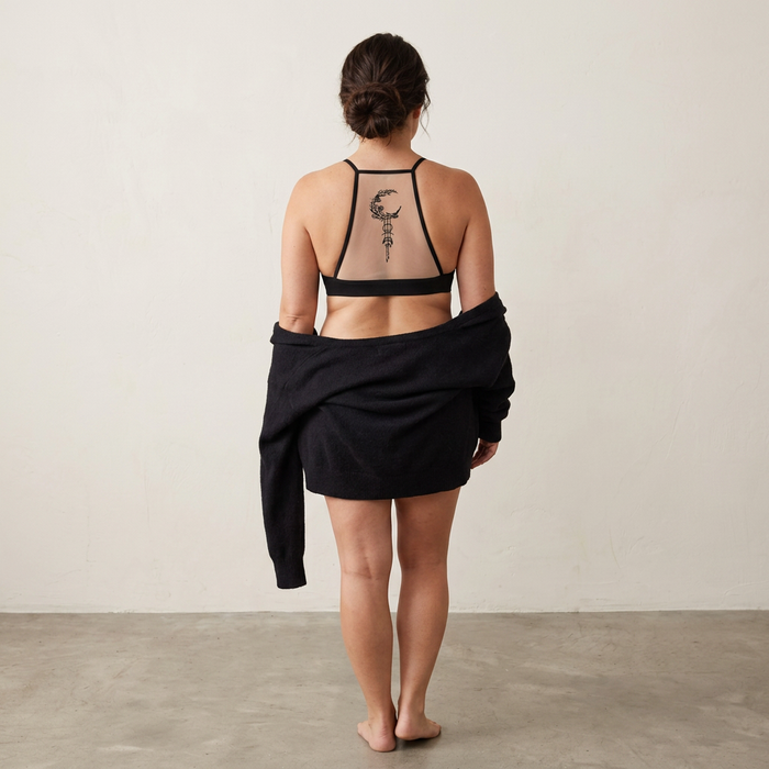 Person wearing a black sports bra and skirt with a tattoo on the back, standing against a plain background.