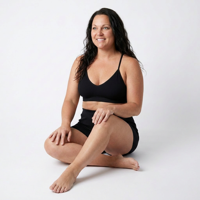 Woman wearing a black sports bra and shorts sitting on a white background