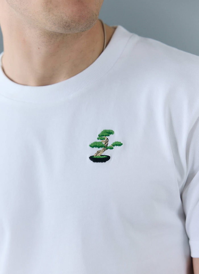 A close-up of a model wearing the white Bonsai T-shirt from Percival, showing the detailed embroidery on the chest.