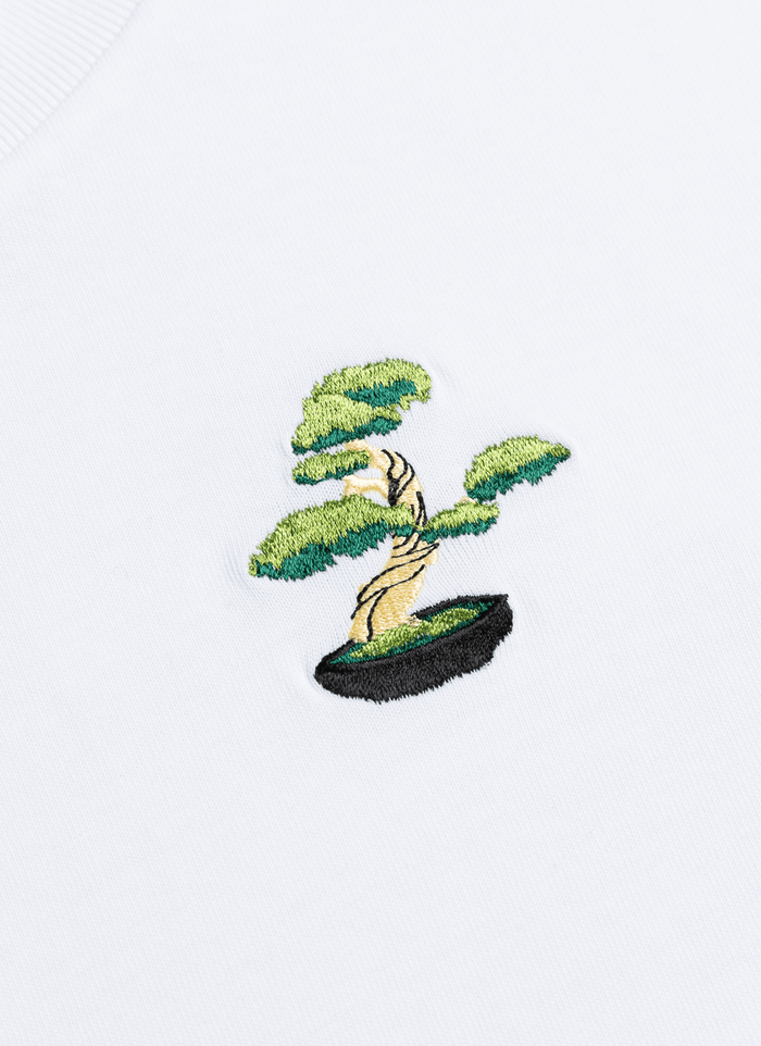 A close-up of the detailed bonsai tree embroidery on the chest of the white organic cotton Bonsai T-Shirt from Percival.