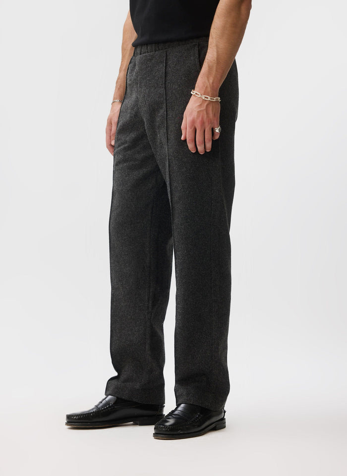 A side profile of a model wearing the black brushed wool Caxton Smart Trousers from Percival with black loafers.