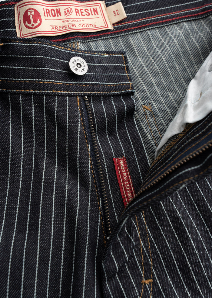 Close-up of Iron and Resin jeans with pinstripes, showcasing a button and label detailing premium quality and size 32.