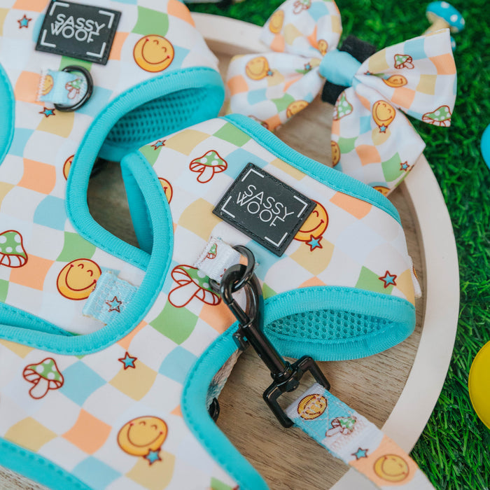 The Dog Adjustable Harness - Mush Love by Sassy Woof features a colorful design with smiley faces, mushrooms, and cupcakes. The set includes a matching leash and bow tie, all perfect for your pet’s stylish outings.
