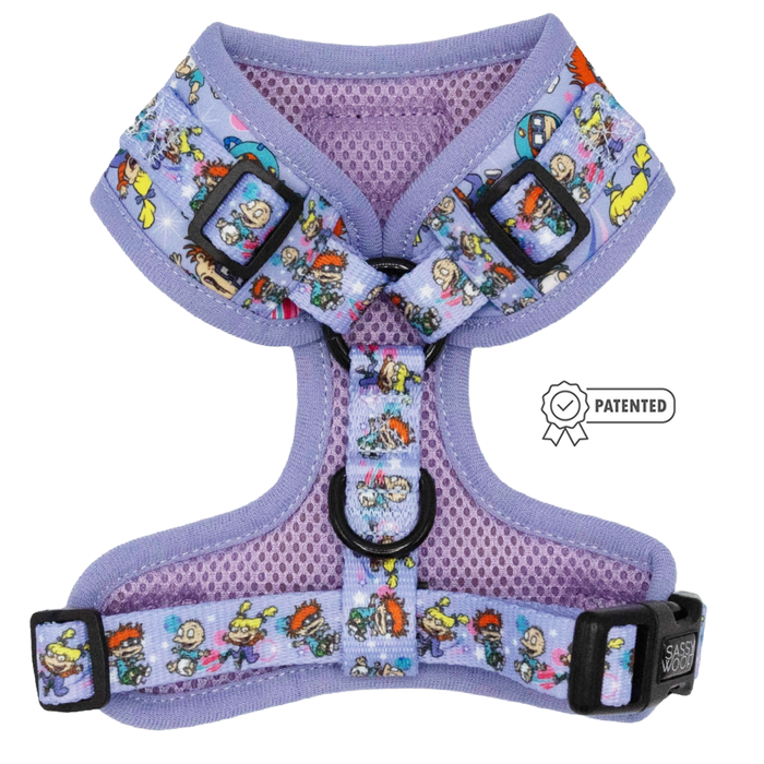 The Sassy Woof Dog Adjustable Harness - Nickelodeon Rugrats™ is a purple mesh harness with black buckles and a colorful cartoon pattern, featuring a patented design badge—ideal for fans of Rugrats dog accessories.
