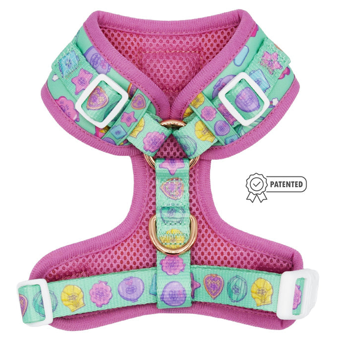 The Sassy Woof Dog Adjustable Harness - Polly Pocket™ features a pink and teal design with cartoon gemstones, white adjustable buckles, a gold leash ring, and a patented badge displayed next to the harness.