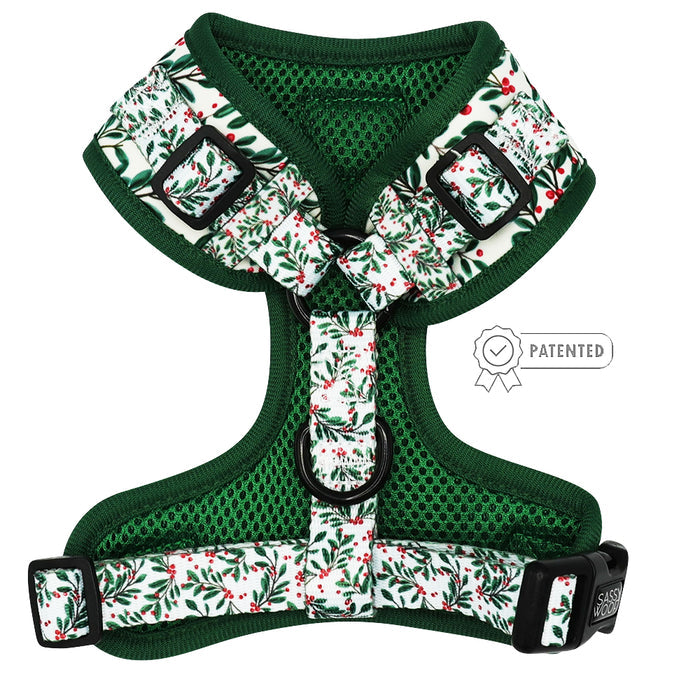 The Sassy Woof Dog Adjustable Harness - Under the Mistletoe features a green design with a white strap showing green leaves and red berries, black plastic buckles, front metal D-ring for no-pull control, and a patented badge beside the harness.