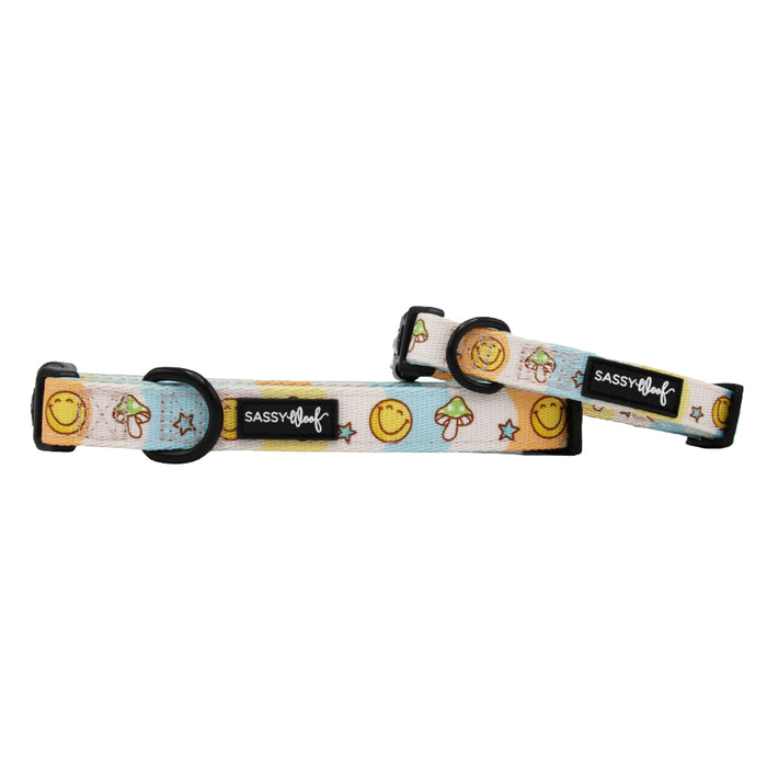 Two "Mush Love" adjustable dog collars by Sassy Woof with black buckles and D-rings. The white/light blue neoprene design features smiley faces, mushrooms, stars, and a black Sassy Woof label.