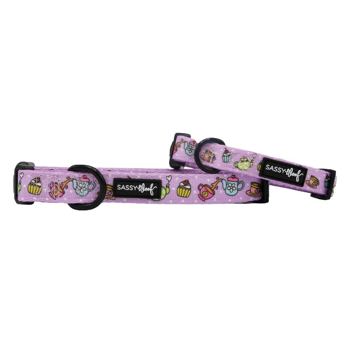 Two "Tea Pawty" dog collars by Sassy Woof in purple with playful cupcake, teapot, and teacup designs. Each neoprene collar has a sturdy D-ring, black plastic buckle, and a black Sassy Woof tag.