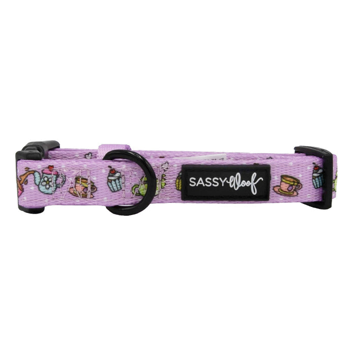 The Sassy Woof Dog Collar - Tea Pawty features a lavender color with tea-themed illustrations, a black buckle, sturdy D-ring for leashes, and a black Sassy Woof label.