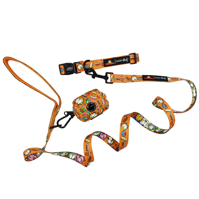 The Dog Collar Three Piece Bundle - Garfield™ by Sassy Woof includes an orange leash, collar, and waste bag holder adorned with playful cartoon dog faces and fun food designs, beautifully arranged on a white background—an ideal set for fans seeking charming Garfield pet accessories.
