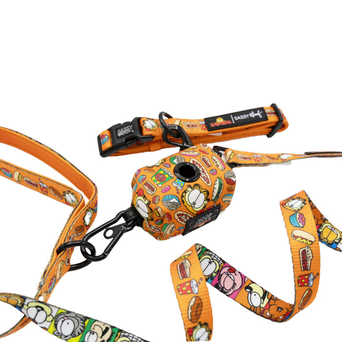 The Sassy Woof Collar Three Piece Bundle - Garfield™ includes an orange collar, leash, and poop bag holder with cartoon food designs on white, black clips, and Sassy Woof branding.