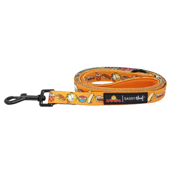 Add a pop of fun to your pet’s style with this orange dog leash from Sassy Woof, decorated with colorful cartoon food designs like hot dogs, popcorn, and drinks. The leash features a sleek black metal clip and branded tags reading “Sassy Woof” and “Central Bark.” Designed as the perfect companion to the “Dog Collar Three Piece Bundle – Garfield™” or other Garfield™ pet accessories for a playful, coordinated look.