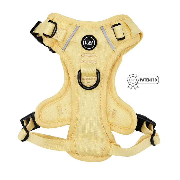 A yellow step-in harness from the Sassy Woof Daffodil Dog Four Piece Bundle features black buckles, a central metal ring, and displays the Patented symbol to the right.