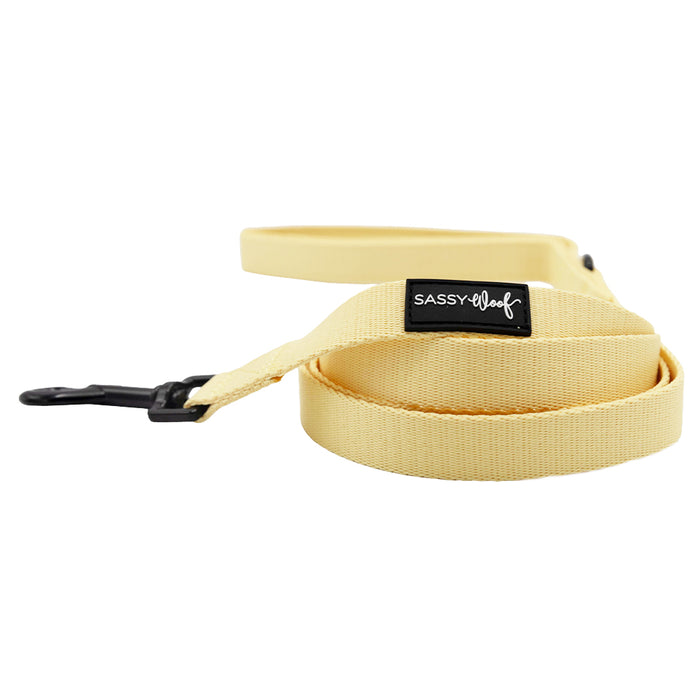 The Sassy Woof Dog Four Piece Bundle - Daffodil includes a pale yellow leash with a black clip, handle, and label. Neatly coiled on a white background—perfect to pair with your step-in harness.