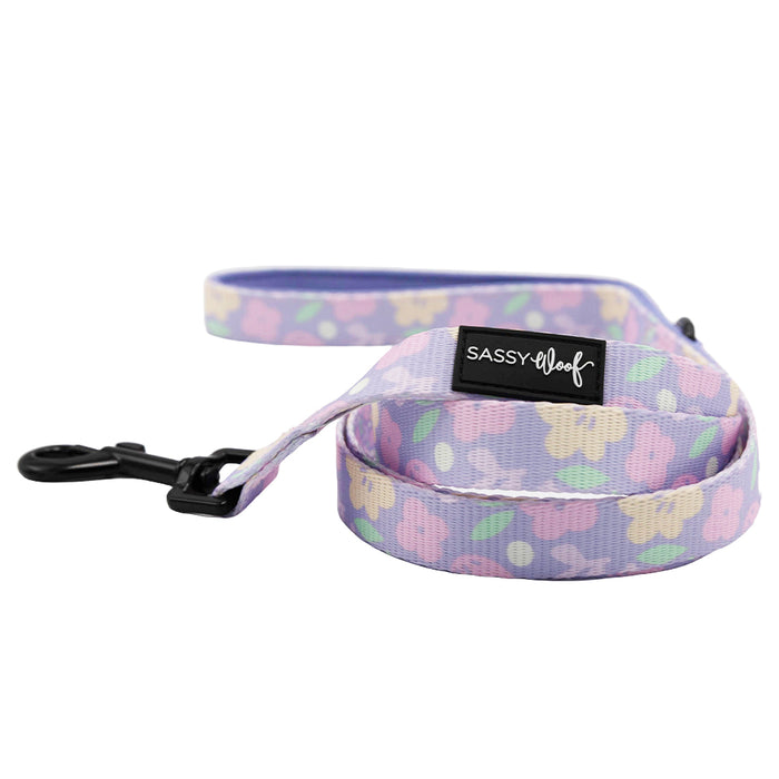 The Sassy Woof Dog Four Piece Bundle - Fleur de Sass features a pastel purple leash with floral pattern, black metal clip, and a black "SASSY WOOF" label—perfect for pairing with an adjustable harness for style and comfort.
