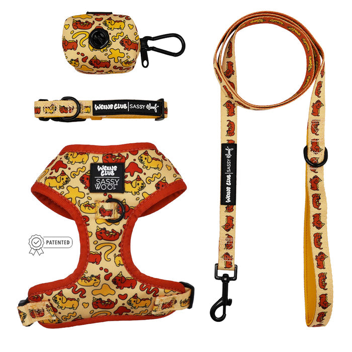 The Sassy Woof Dog Four Piece Bundle - Hot Dawg features an adjustable harness with orange trim, leash, waste bag holder, and collar. All are yellow with red cartoon dog and bone patterns, plus a black Sassy Woof patch—displayed on a white background.