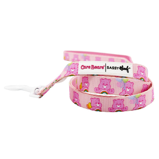 The Sassy Woof Dog Leash - Care Bears™ Cheer Bear features pink Care Bears and rainbows, a white clasp, and branded tag—perfect to pair with your pup's matching harness for extra cuteness on walks.
