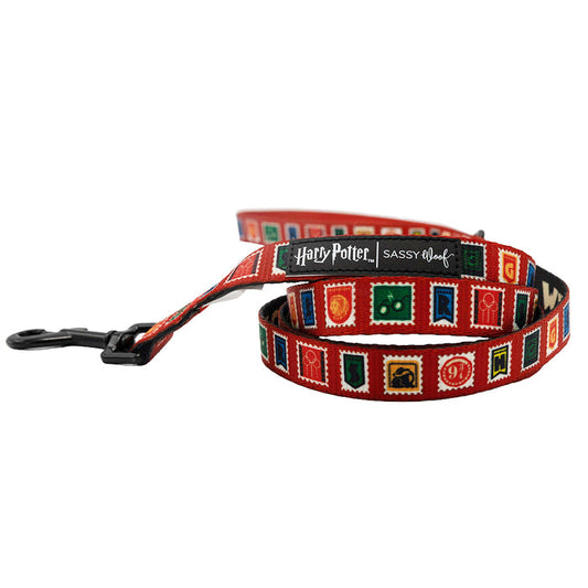 The Sassy Woof Dog Leash - Harry Potter™ Stamps is a red leash decorated with colorful magical stamps and symbols, a black clip, and a “Harry Potter Sassy Woof” label from the Harry Potter™ collection.