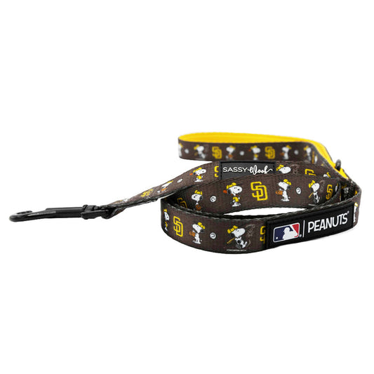 The Sassy Woof Dog Leash - MLB™ x Peanuts™ San Diego Padres™ features brown Peanuts and Padres designs, a yellow underside, Snoopy accents, and logos near the black metal clasp.