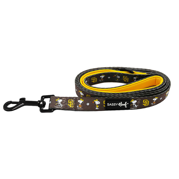 The Sassy Woof Dog Leash - MLB™ x Peanuts™ San Diego Padres™ features Snoopy and Padres logos on a brown background, a yellow inner layer, white Sassy Woof branding, and a black metal clip.