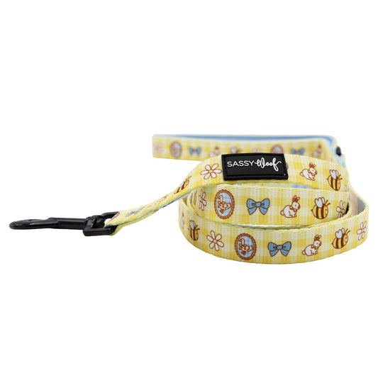 The Sassy Woof Dog Leash - Patch Perfect features yellow neoprene, playful cartoon bees, bows, flowers, teddy bears, a black clip, and brand label—perfect for fun-loving pups.