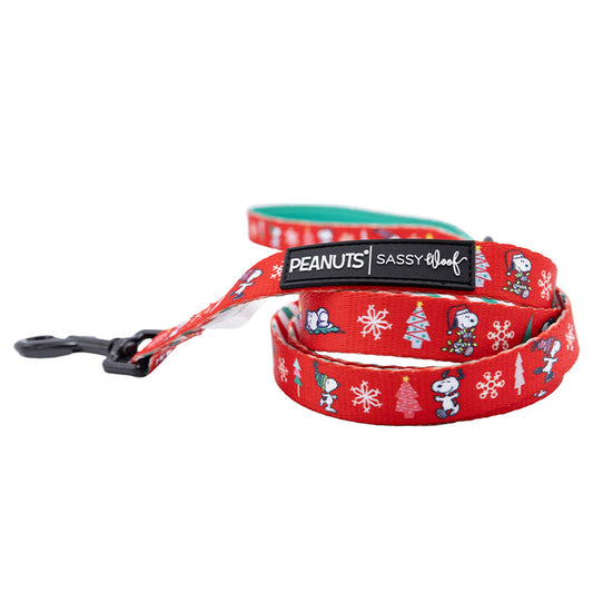The Sassy Woof Dog Leash - Peanuts™ Beagle Bells features Snoopy, Woodstock, Christmas trees, and snowflakes. This festive leash has a black metal clasp and a “PEANUTS | SASSY WOOF” label—perfect for the holidays!.