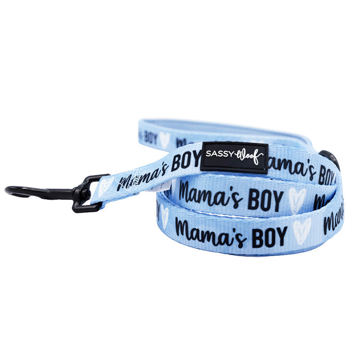 A light blue leash from the Sassy Woof Dog Three Piece Bundle - Mama's Boy, with black hardware, “Mama’s BOY” text, white heart designs, and a black patch featuring the Sassy Woof brand name.