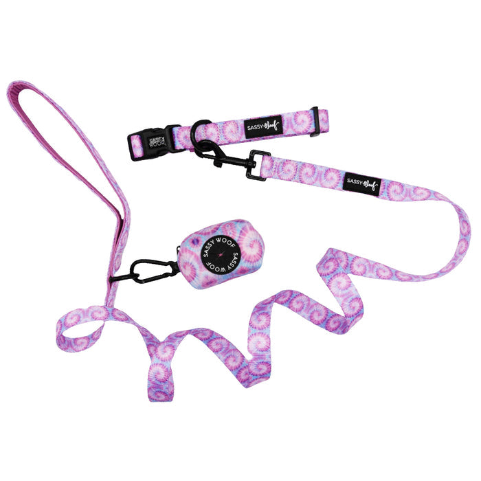 The Sassy Woof Dog Three Piece Bundle - Purple Haze includes a pink and white tie-dye leash, matching collar, and black waste bag holder, all displayed on a white background.