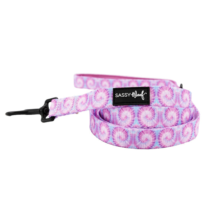 The Sassy Woof Dog Three Piece Bundle - Purple Haze features a pink and purple tie-dye patterned leash with a black metal clip and Sassy Woof label, perfectly matching the Purple Haze dog collar. The set comes neatly coiled.