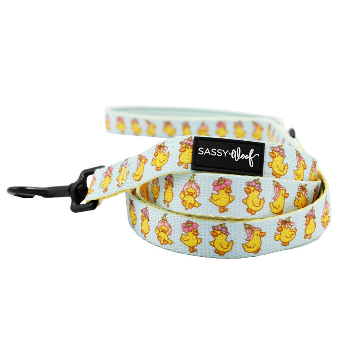 The Sassy Woof Dog Two Piece Bundle - Good Duck, Babe! includes a light blue leash with yellow ducks in pink bows and matching harness for a coordinated look. Features a black clasp and “Sassy Woof” label.