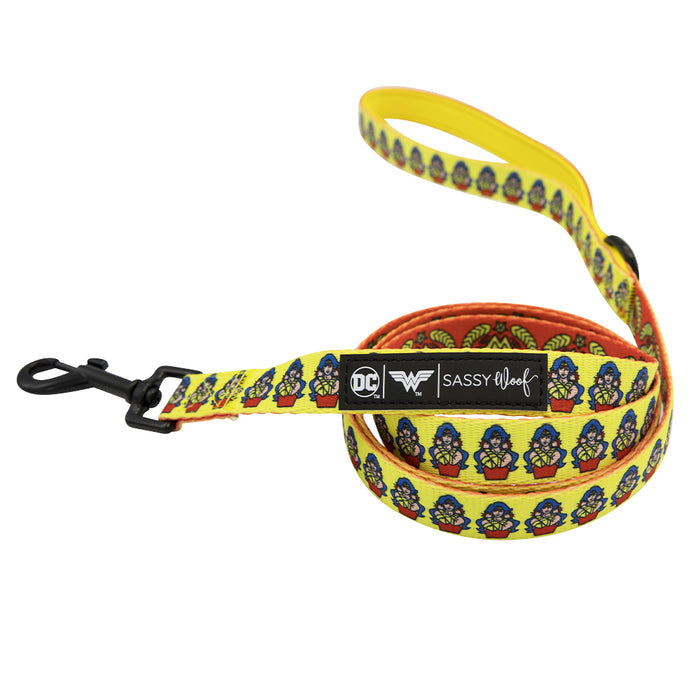 A yellow adjustable dog leash from the Dog Two Piece Bundle - Wonder Woman™ by Sassy Woof, featuring a repeating cartoon Wonder Woman pattern, black metal clasp, and a label with DC x Sassy Woof and Wonder Woman logos.