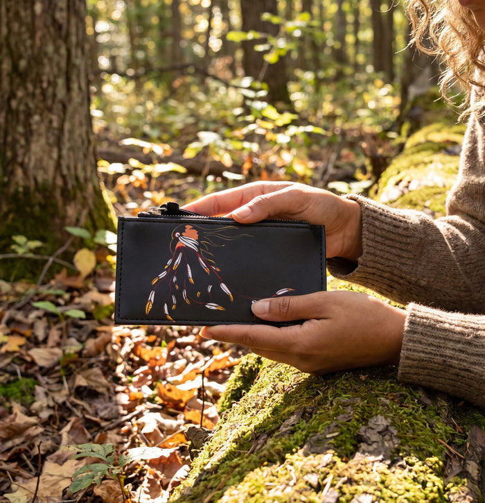 Person holding a black wallet with a colorful design in a forest setting