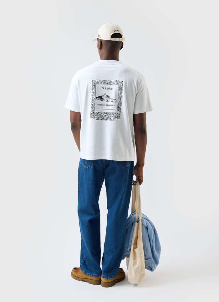 A model seen from behind wearing the white Percival Ex Libris oversized t-shirt, showing the back graphic print.