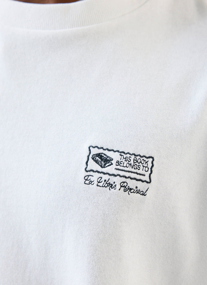 A close-up shot of the bookplate-style 'Ex Libris' embroidery on the chest of a white t-shirt from Percival.