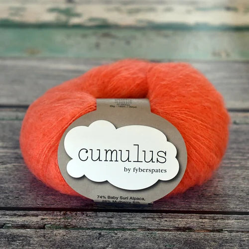 Orange skein of yarn with 'cumulus' label on a wooden surface