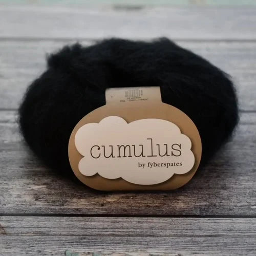 Black yarn ball with 'Fyberspates cumulus' label on a wooden surface