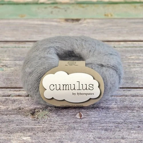 Gray skein of yarn with 'Fyberspates cumulus' label on a wooden surface