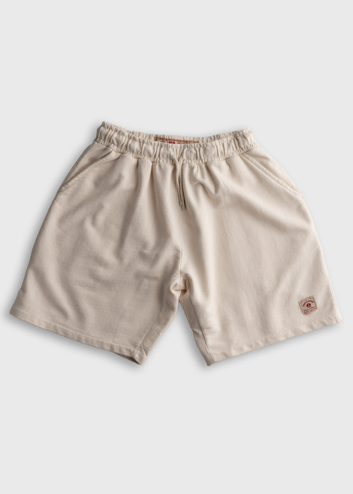 Beige cotton shorts with elastic waistband and small logo patch on the hem, displayed on a plain white background.