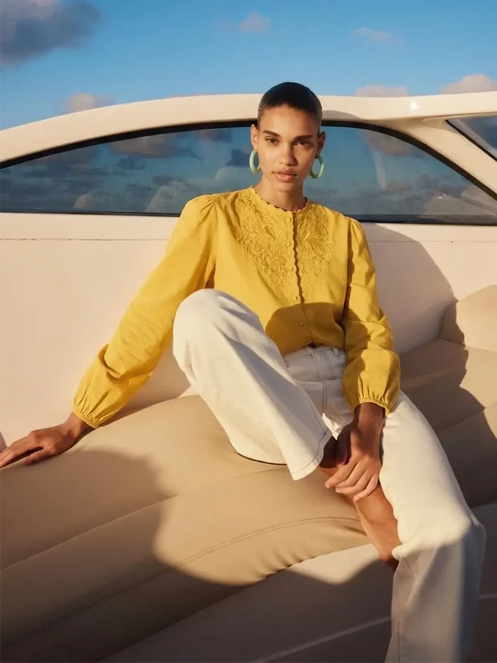 Person wearing a yellow top and white pants sitting on a boat.