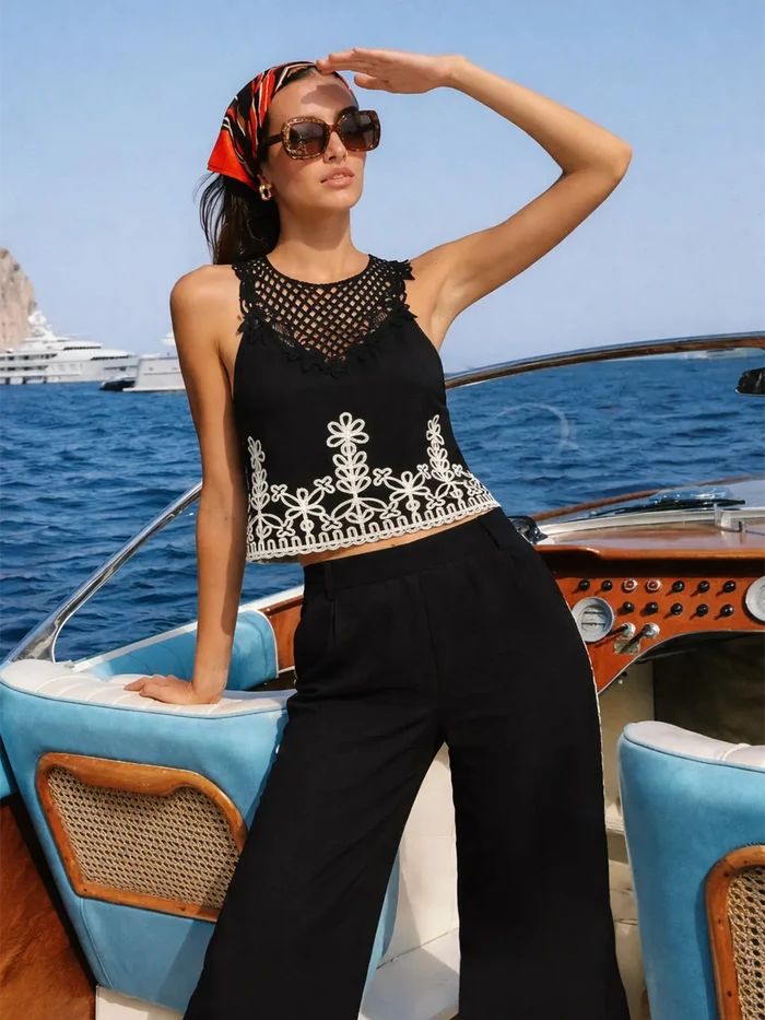 Woman on a boat wearing a black sleeveless top with white embroidery and black pants, with a scenic background.