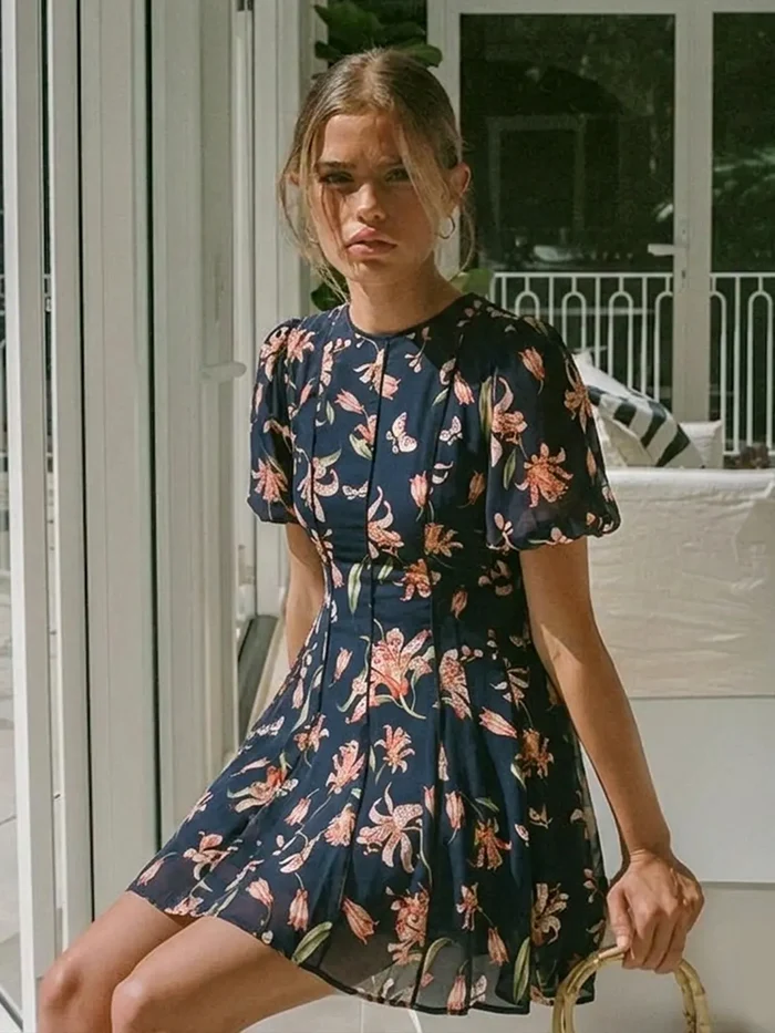 Woman wearing a navy floral dress sitting on a chair.