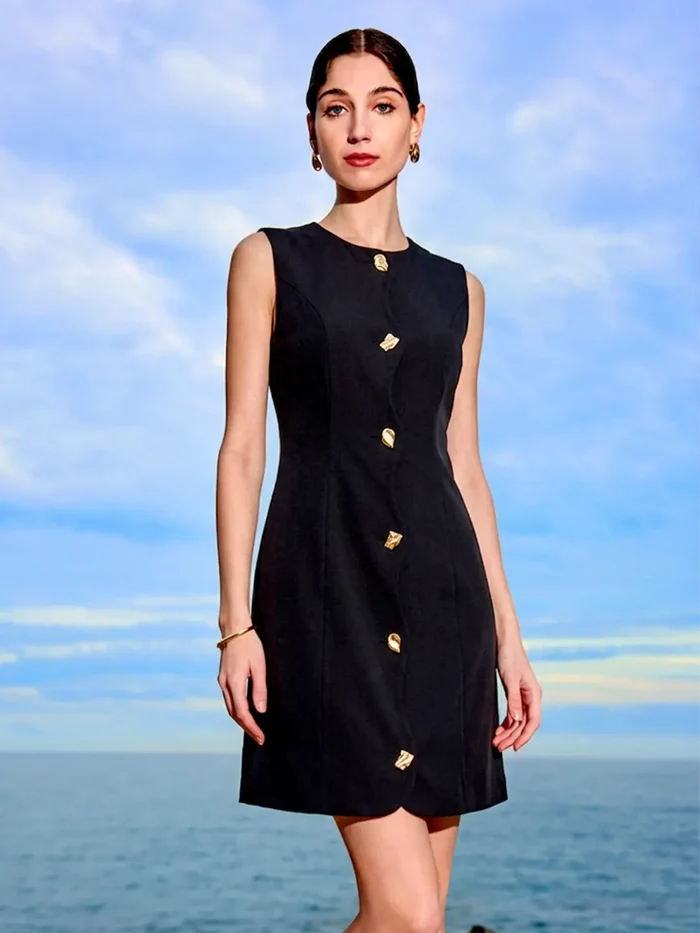 Woman wearing a black dress with gold buttons against a blue sky and ocean background
