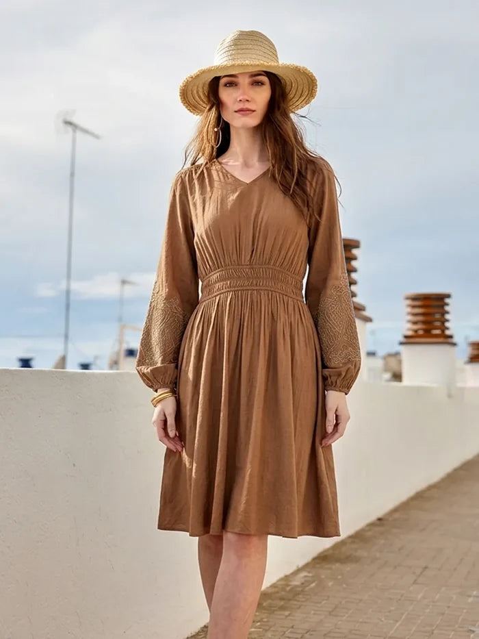 Woman wearing a brown dress and straw hat on a rooftop with a clear sky.