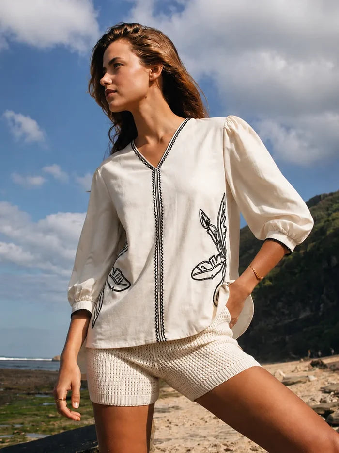 Woman wearing a white blouse with black embroidery on a beach