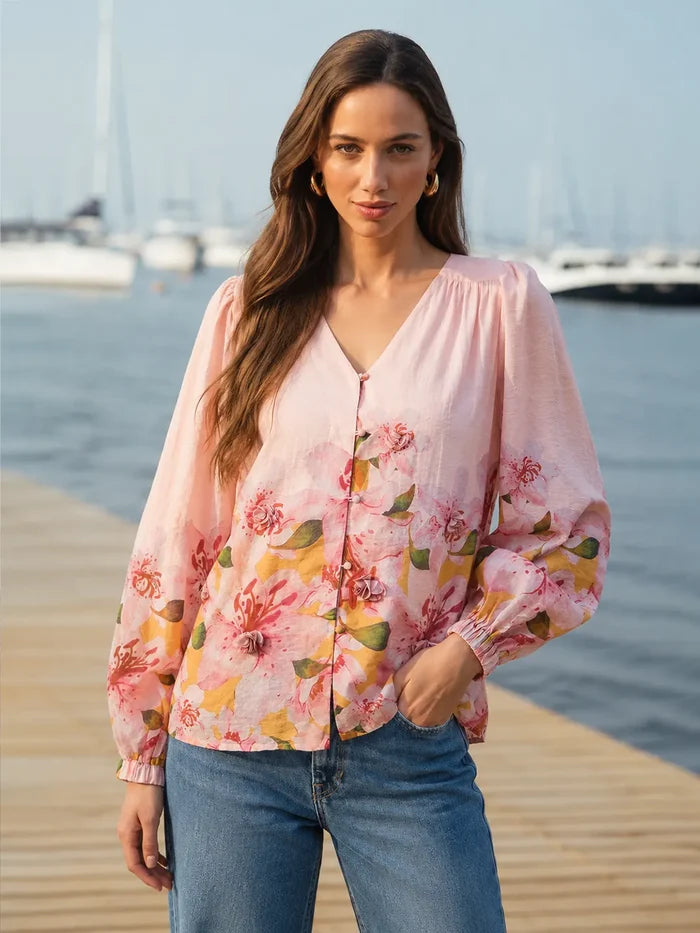 Woman wearing a pink floral blouse and blue jeans by a waterfront.