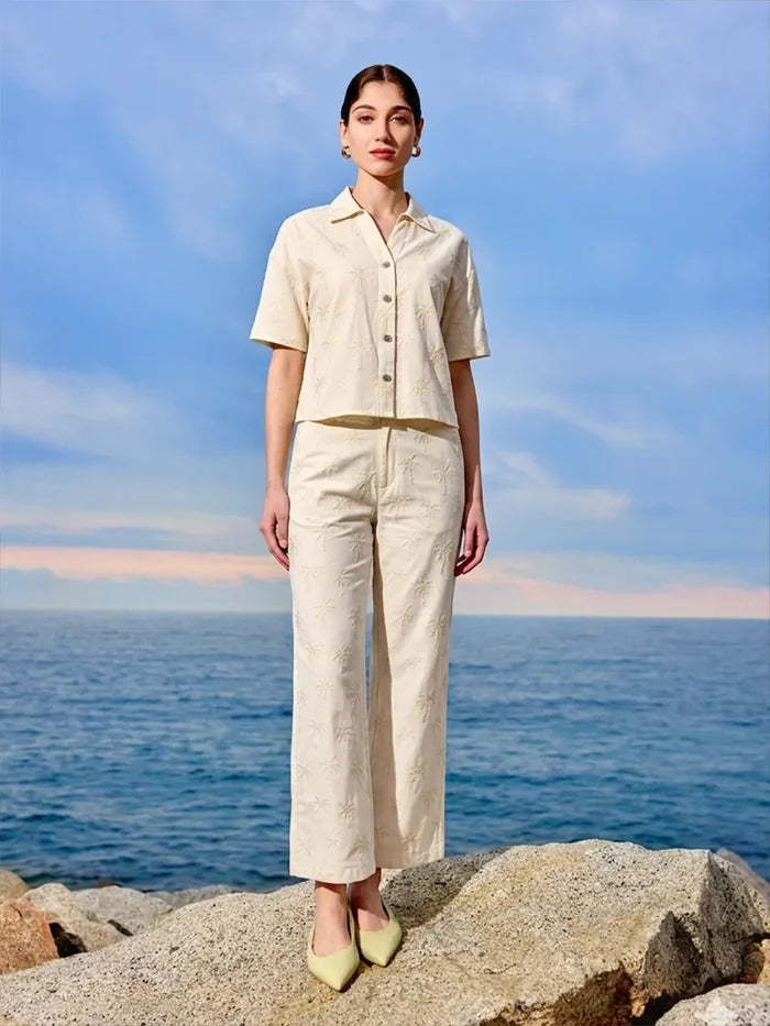 Woman in a beige outfit standing on rocks with ocean and sky in the background