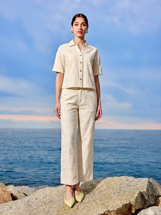 Woman in a beige outfit standing on rocks with ocean and sky in the background