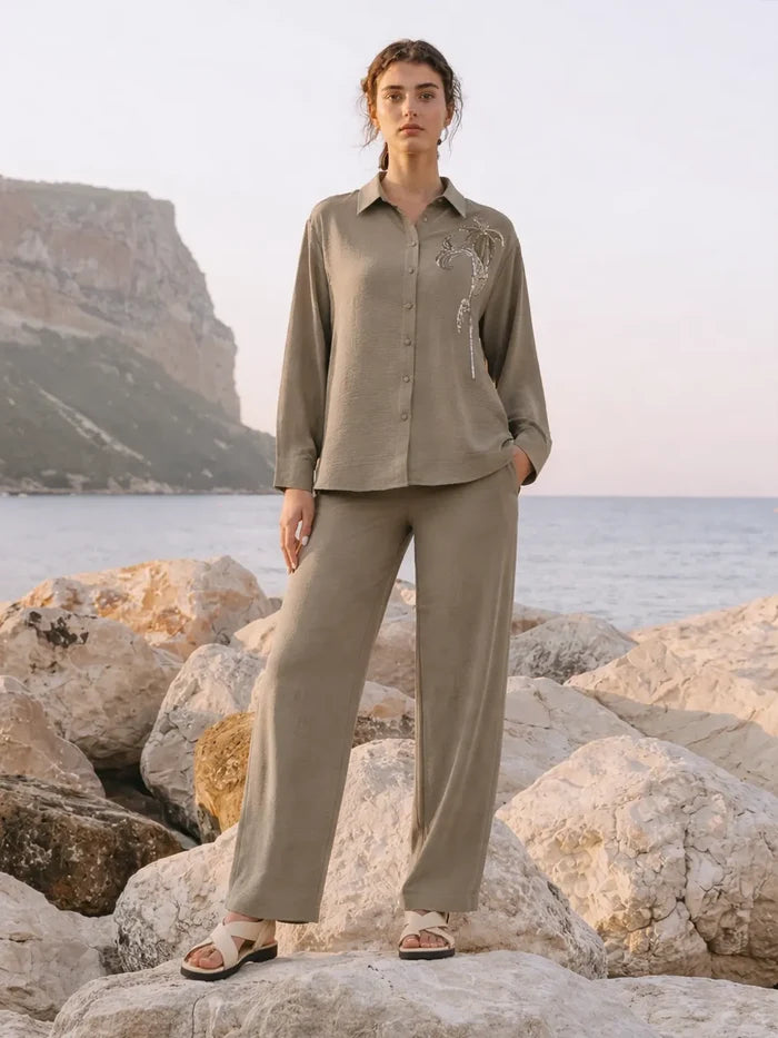 Woman in a beige outfit standing on rocks by the sea