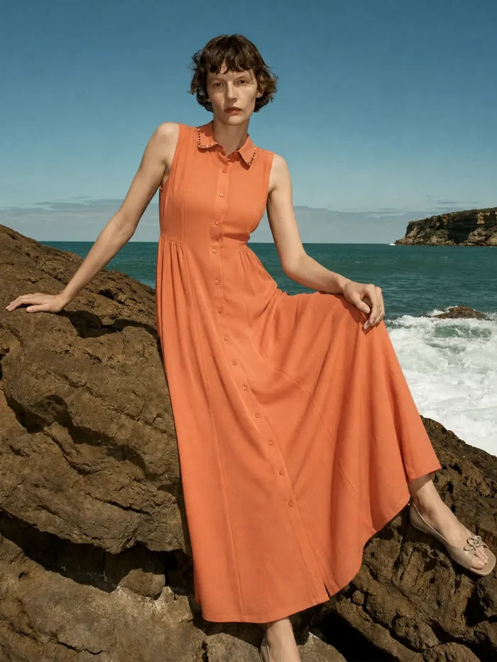 Woman in an orange dress standing on a rocky beach with ocean and sky in the background